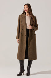 A woman is wearing a long, brown, double-breasted wool coat with a tailored fit, wide lapels, and flap pockets. Underneath, she has on a light beige knit sweater. She pairs this with black pants and black high-heeled knee-high boots.